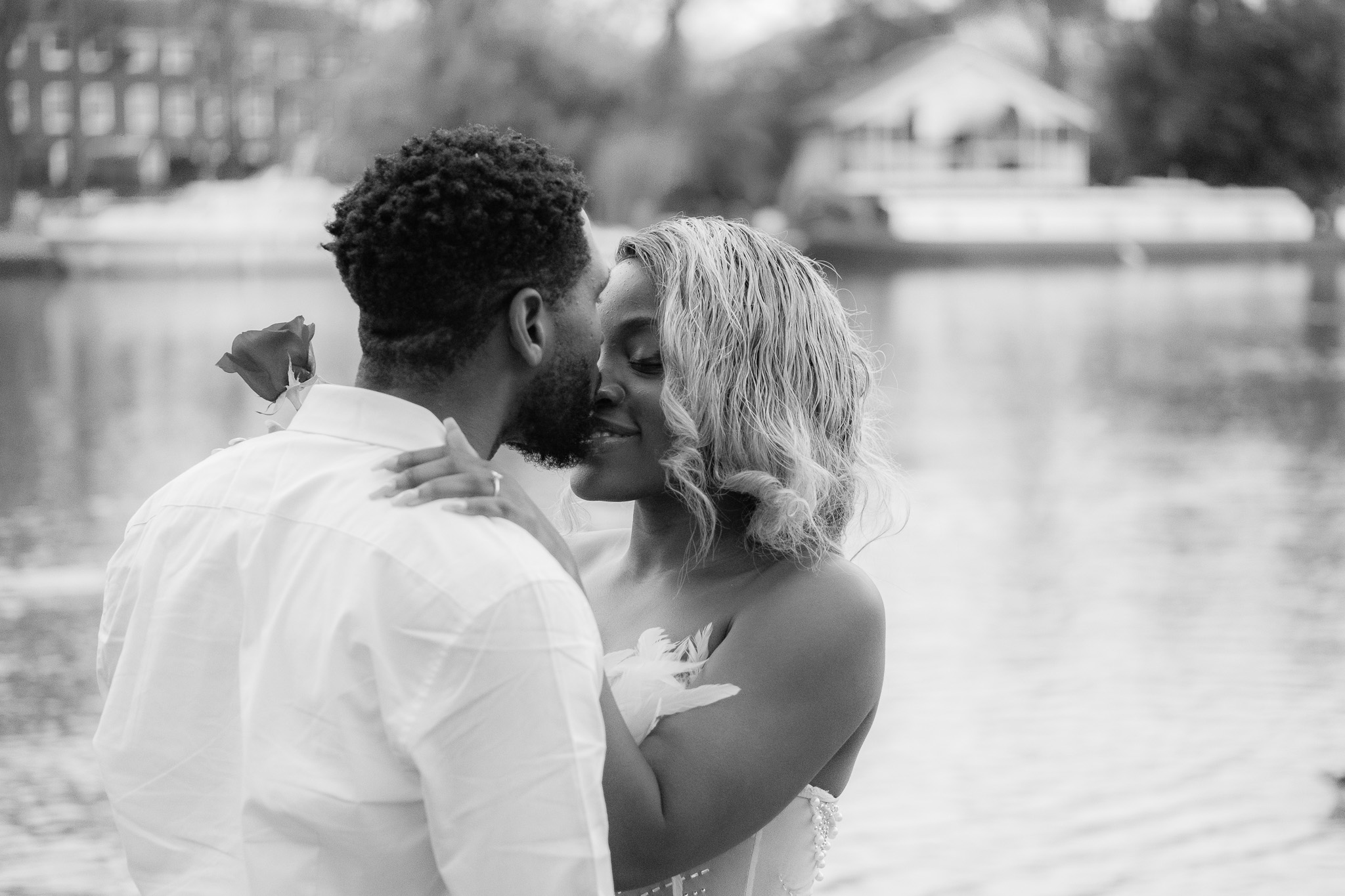 Couple by the river, woman is holding a rose and the man is kissing her on the nose