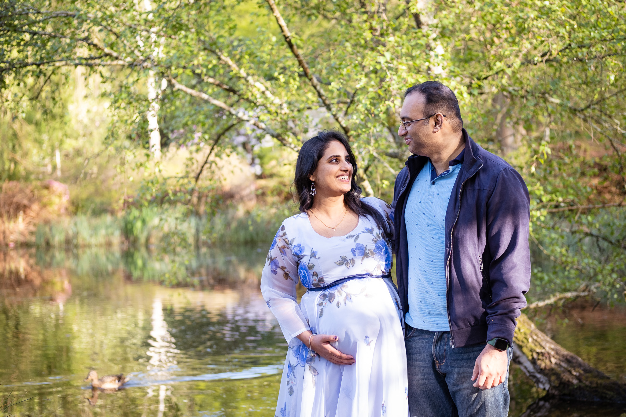 Pregnant woman looking at her husband romantically, surrounded by serene lake and flowers