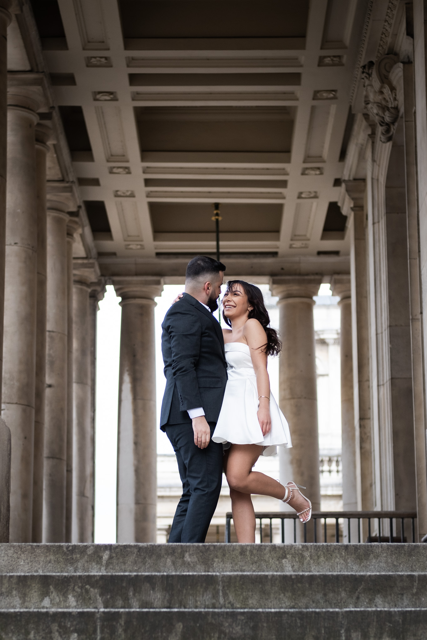 Couple posing in front of stairs in Greenwich, man is kissing the woman