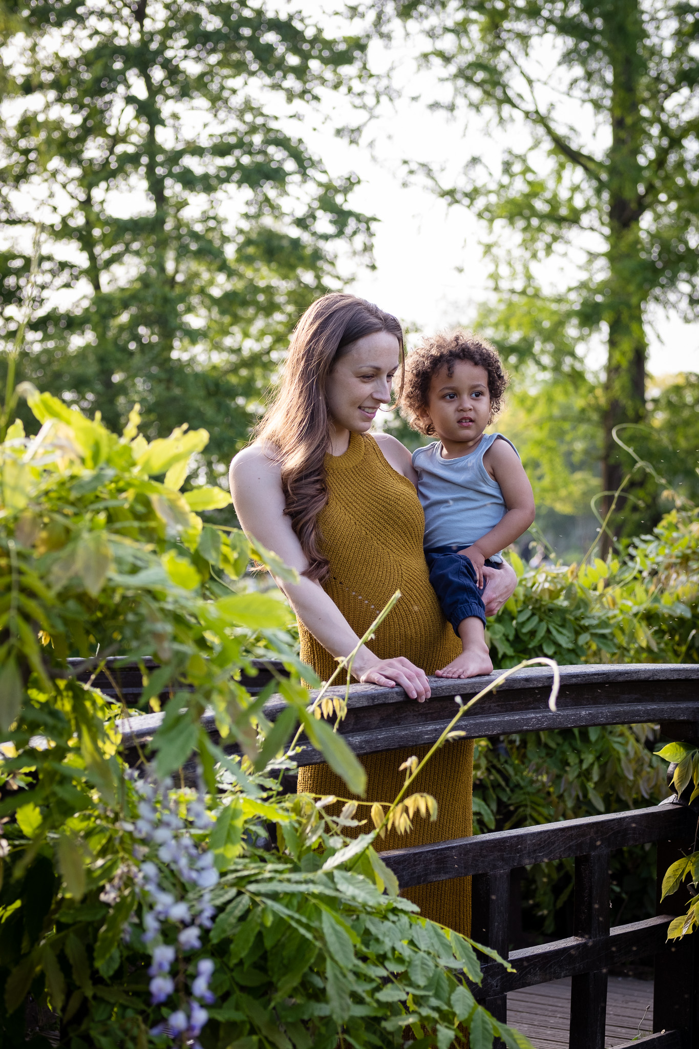 Mother and her small toddler, looking in front of them where there is a small wooden bridge 
