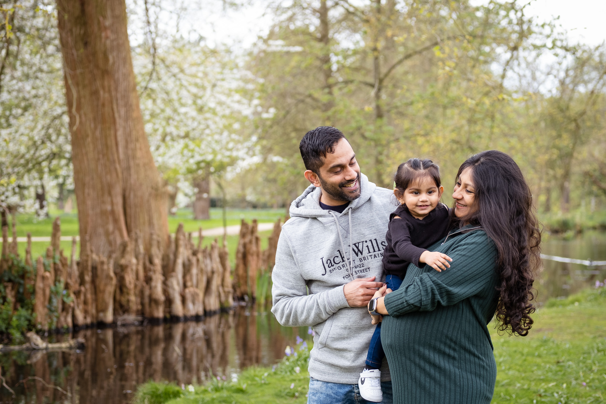 Young family holding their child smiling and having good time in London's best parks (Bushy park)