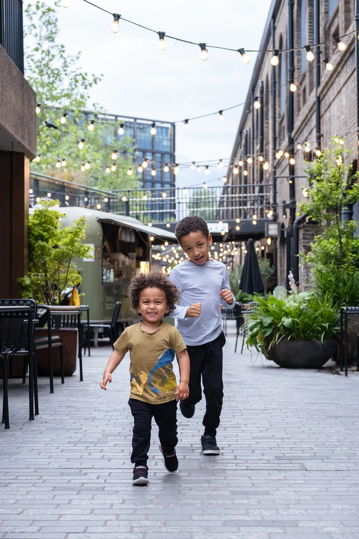 Two brothers running and playing together on a street with lights