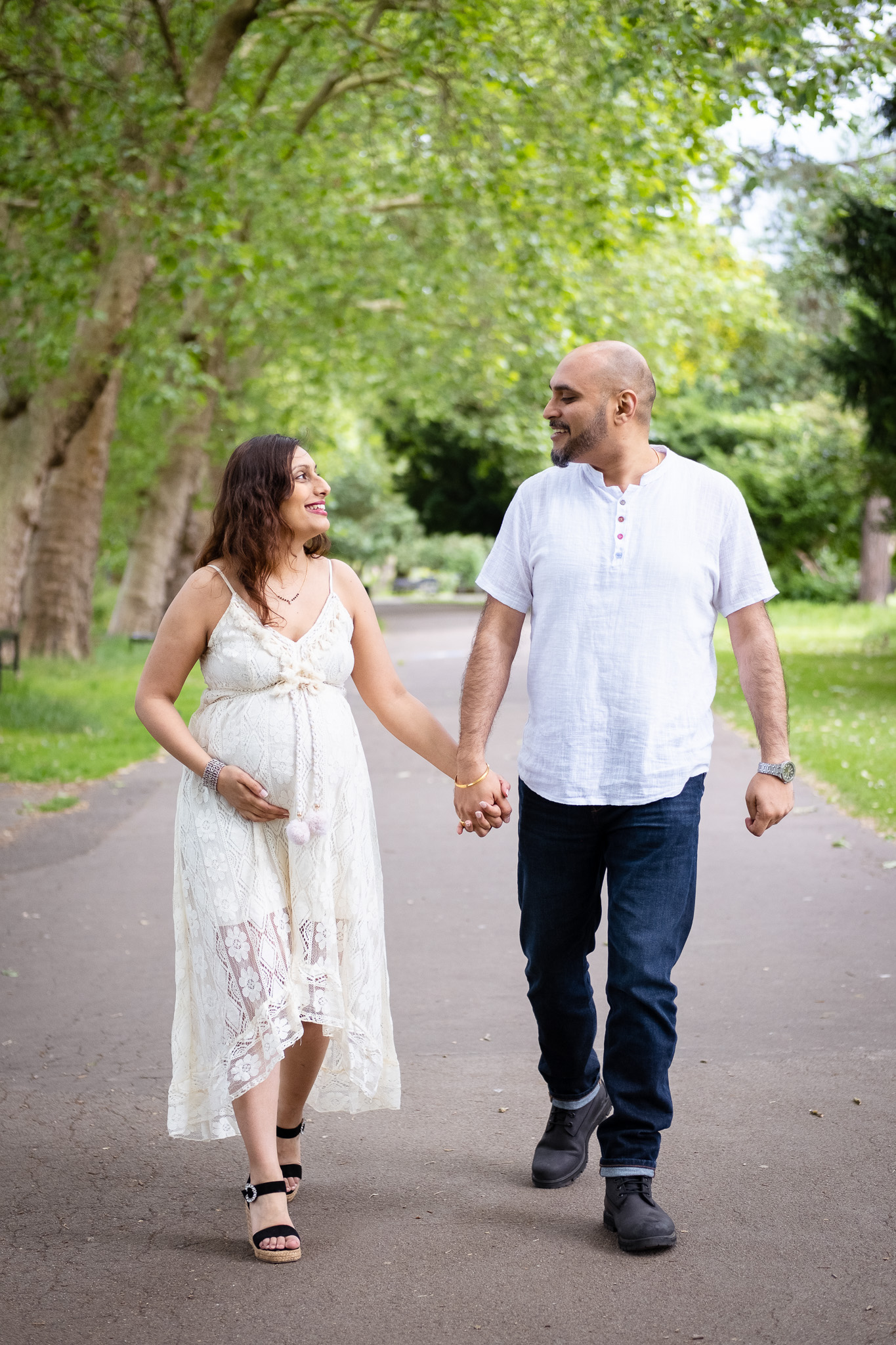 Pregnant woman and man holding hands, walking on a nice path way on a sunny day