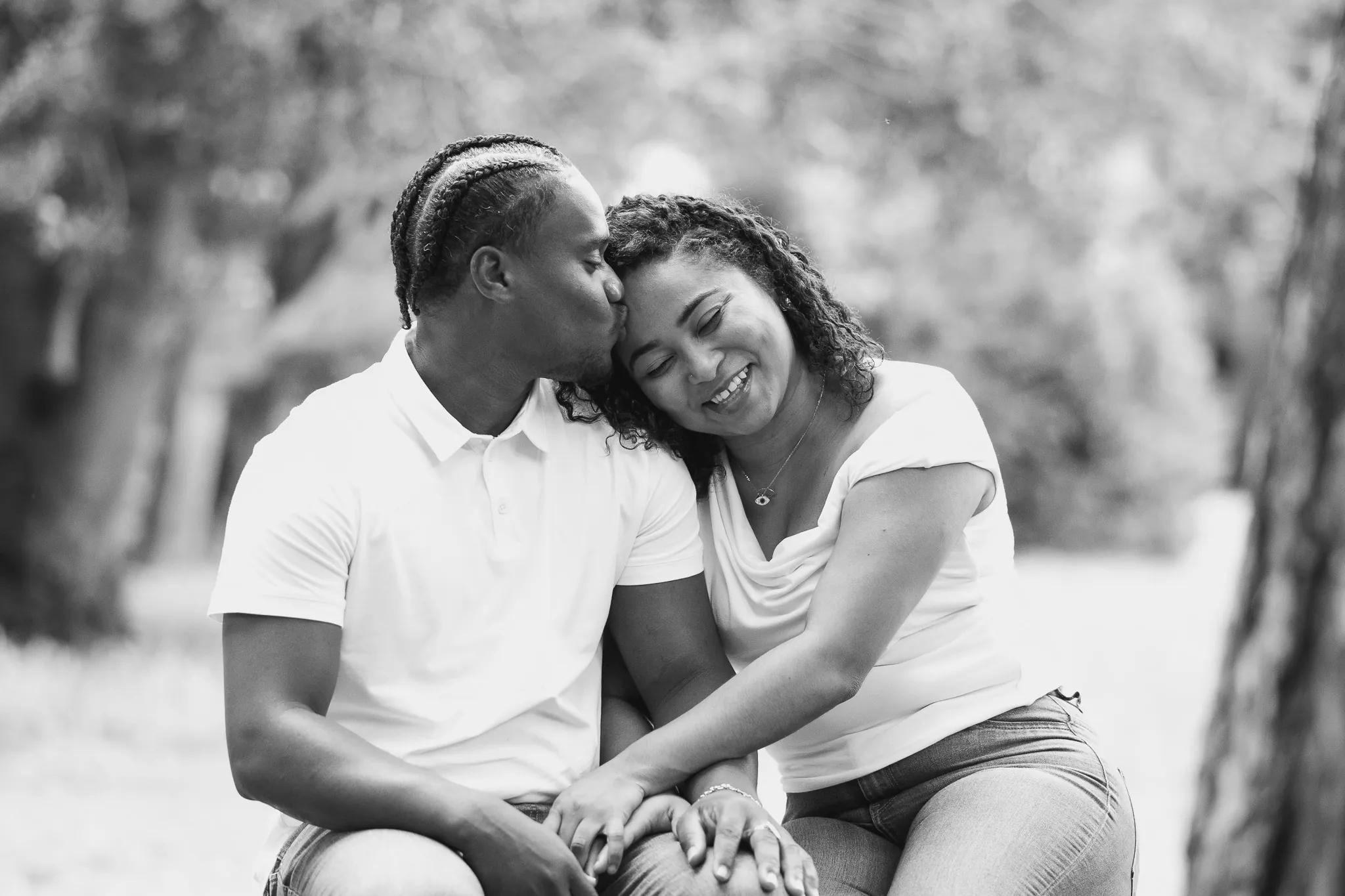 Man kissing his girlfriend on her head, in love sitting in a park